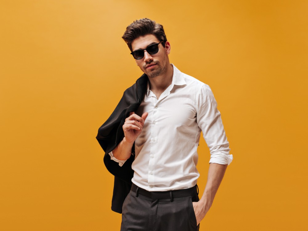 Attractive Brunet Man Stylish White Shirt Trendy Sunglasses Poses Orange Background Holds Black Jacket